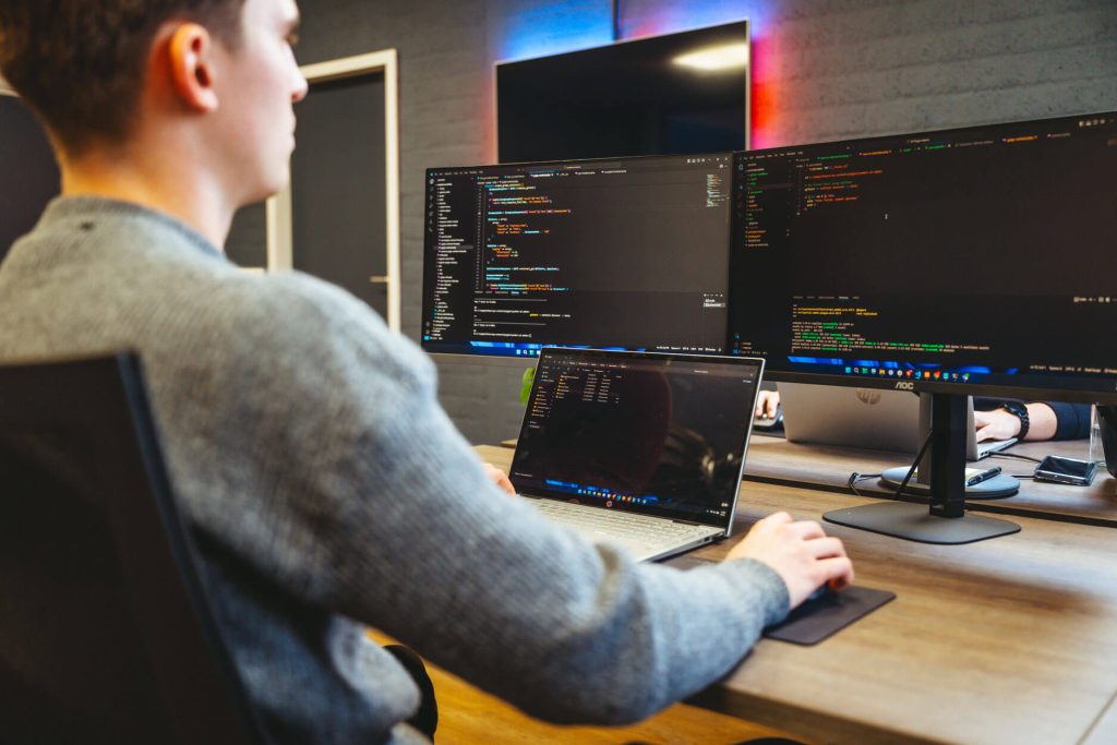 Programmeur werkt aan computer met code op schermen