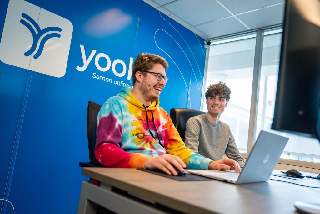 Twee mannen werken lachend samen aan laptop.