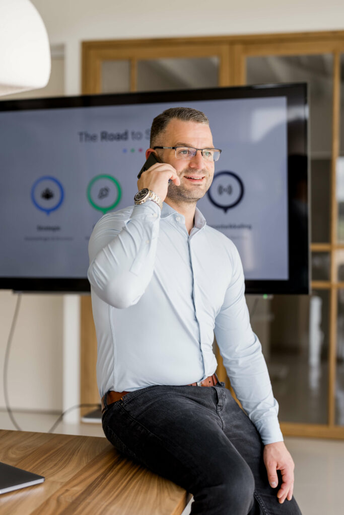 Eric belt zittend aan tafel met scherm op achtergrond.
