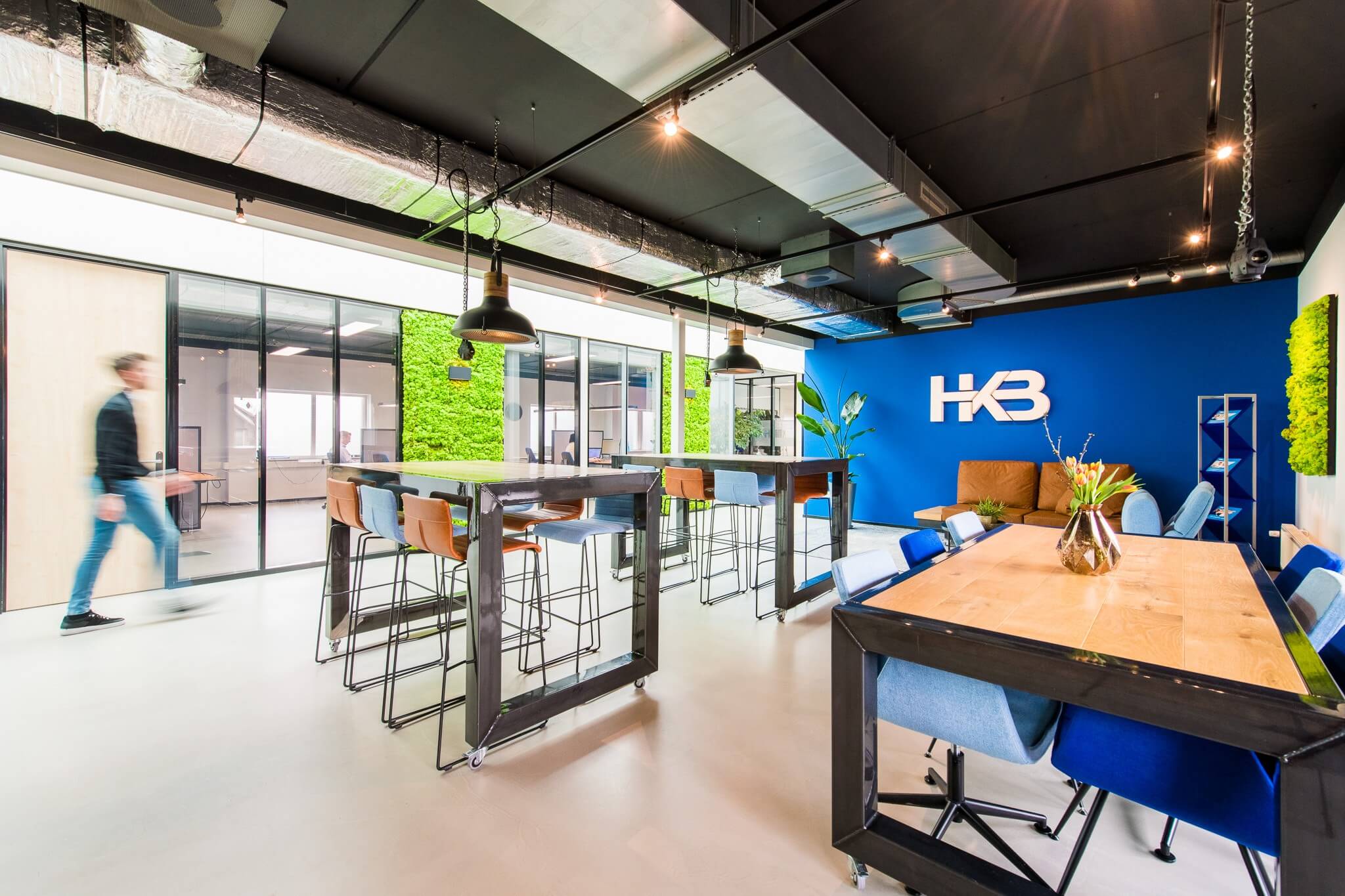 Moderne kantoorruimte met plantenwand en blauwe stoelen.